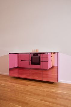 an empty kitchen with pink cabinets and wood flooring in front of a white wall