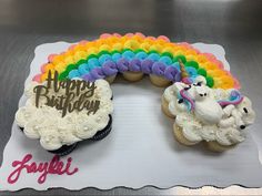 two cupcakes with white frosting and rainbow decorations