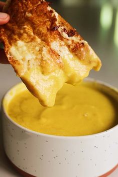 a person dipping cheese into a bowl of soup with a piece of bread in it