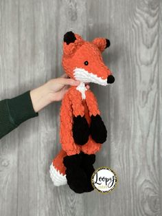 a person is holding a stuffed animal that looks like a red fox with black legs