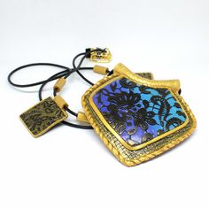 a blue and black square shaped pendant with gold accents on a cord that is attached to a white background