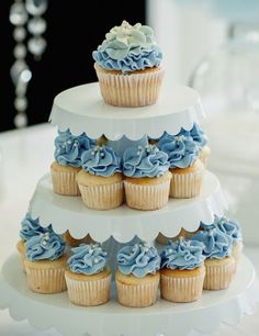 a three tiered cake with blue frosting and cupcakes on the top