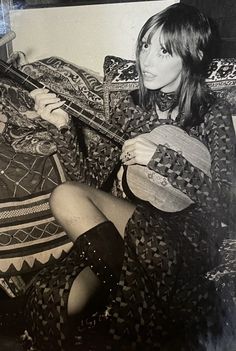 a black and white photo of a woman sitting on a couch with a guitar in her hand