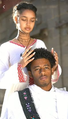 a young man getting his hair cut by a woman in an african style dress and head piece