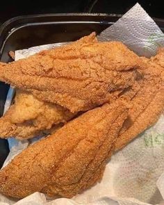 two fried fish fillets sitting on top of a piece of paper in a container