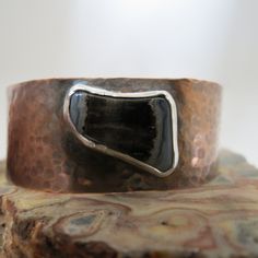 Elevate your style with our handmade Petrified Wood in Copper Cuff bracelet. The unique polished black stone with white detailing at the edges adds a touch of sophistication to any outfit. The cuff is 7/8" wide, from a 6" piece of copper, and the stone is 3/4" x 1/2." The cuff is adjustable and the edges are rounded for wearability and comfort. Artisan Adjustable Black Cuff Bracelet, Rustic Black Bracelets As A Gift, Rustic Black Bracelets As Gift, Handmade Black Cuff Bracelet, Rustic Black Bracelet For Gift, Rustic Black Bracelet Perfect For Gifting, Black Artisan Handmade Cuff Bracelet, Handmade Artisan Black Cuff Bracelet, Artisan Handmade Black Cuff Bracelet