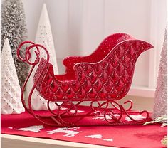 a red sleigh sitting on top of a wooden table next to christmas trees