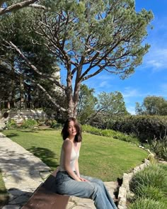 a woman sitting on top of a wooden bench next to a tree