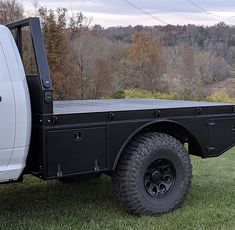 the back end of a white truck parked on top of a lush green field with trees in the background