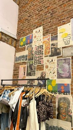 clothes hanging on racks in front of a brick wall covered with posters and pictures,