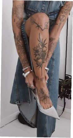 a person with tattoos on their legs and feet, holding onto a pair of high heels