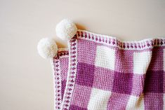 two crocheted dishcloths with pom - poms hanging from them