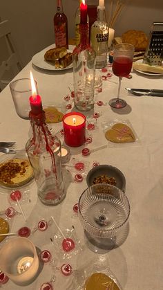 a white table topped with lots of plates and glasses filled with food next to candles