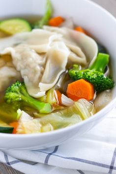 a white bowl filled with dumplings and veggies on top of a table