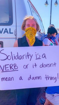 a woman holding a sign that says solidarity is a verbb or it doesn't mean a damn thing