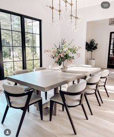 a dining room table surrounded by chairs and a vase with flowers on it in front of a large window