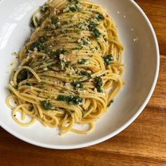 a white bowl filled with pasta covered in pesto and parmesan cheese on top of a wooden table