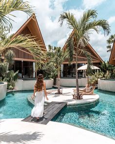 a woman walking across a wooden walkway next to a pool with palm trees in the background