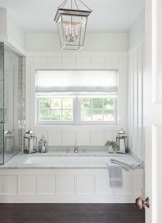 a white bathroom with a large tub and window above it is lit by a pendant light