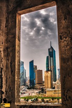 an open window looking out onto a city with tall buildings in the distance and cloudy sky