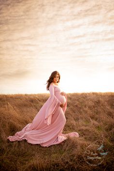 a pregnant woman in a pink dress sitting on the ground with her belly wrapped up