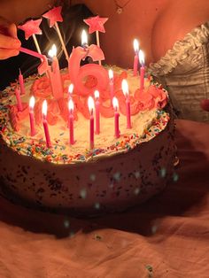 a woman blowing out candles on a birthday cake with pink frosting and sprinkles