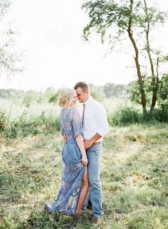 a man and woman are standing in the grass with their arms around each other as they look at each other