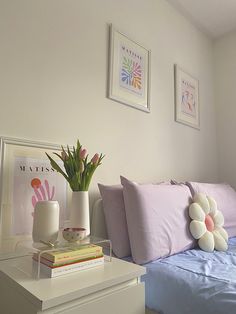 a bed with pink and white pillows on top of it next to two vases filled with flowers