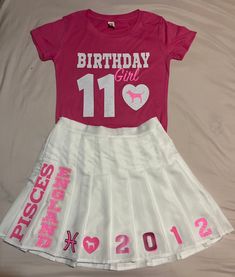 a pink birthday shirt and white skirt on top of a bed next to each other