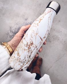 a person holding a white and gold marbled water bottle