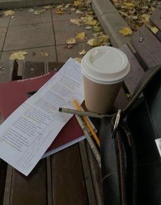 a cup of coffee sitting on top of a wooden bench next to a pile of papers