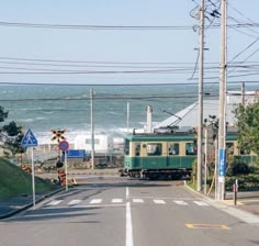 a green train traveling down tracks next to the ocean with power lines above and below it