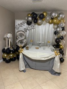 a table topped with balloons and a white table cloth covered in black and gold decorations