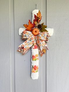 a cross made out of fabric with fall leaves and pumpkins hanging on the front door