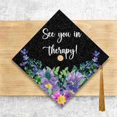 a graduation cap that says see you in therapy with purple flowers and greenery on it