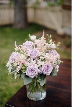 a glass vase filled with purple flowers on top of a wooden table next to grass