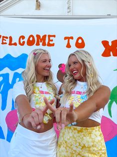 two women pointing at something while standing in front of a welcome sign