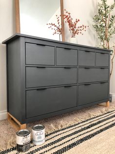 a gray dresser with two paint cans on the floor next to it and a mirror