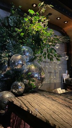 a vase filled with lots of green plants on top of a wooden table next to a mirror ball