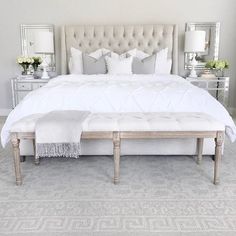 a large white bed sitting in a bedroom next to a dresser and mirror on the wall