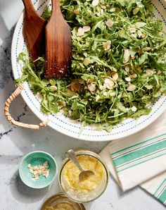 a salad in a bowl with two wooden spoons on the side and some other ingredients around it