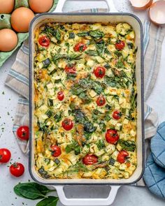 an egg casserole with spinach and tomatoes in a baking dish next to eggs