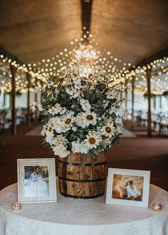 a wooden barrel filled with white flowers sitting on top of a table next to two pictures