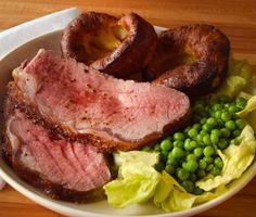 a white bowl filled with meat and vegetables on top of a wooden table next to a napkin