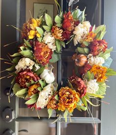 a wreath is hanging on the front door with flowers and leaves around it in fall colors