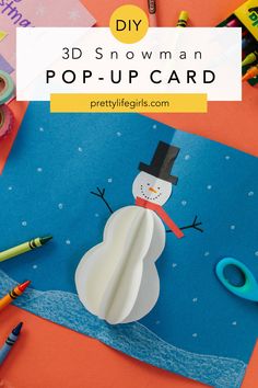 a snowman pop - up card with crayons and markers on the table