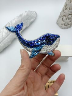 a hand is holding a blue and white whale brooch with pearls on it's tail