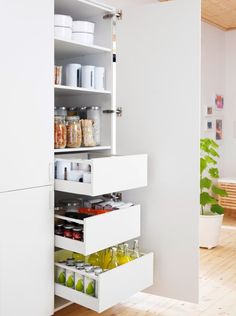 an organized pantry in the corner of a room with white cupboards and open drawers