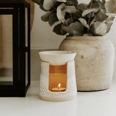 a candle is sitting on a table next to a vase with a plant in it