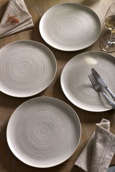 four white plates and silverware on a wooden table